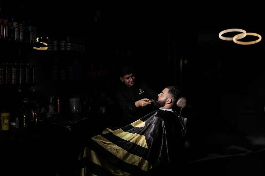 Professional barber trimming a client beard in a dark luxury barbershop with gold cape and lighting in Warragamba.